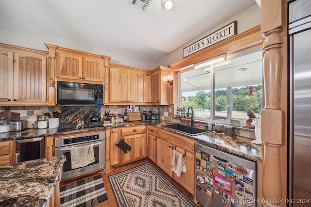 kitchen with appliances with stainless steel finishes, dark stone countertops, sink, and tasteful backsplash