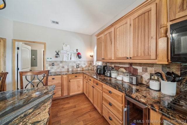 kitchen with light brown cabinets, beverage cooler, light hardwood / wood-style flooring, backsplash, and dark stone countertops