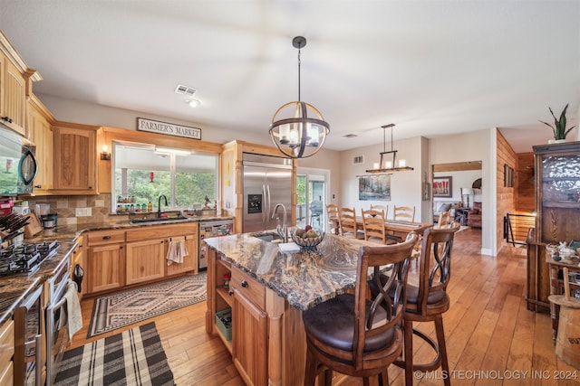 kitchen with dark stone counters, light wood-type flooring, sink, stainless steel appliances, and a center island with sink