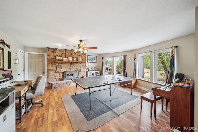 playroom with light wood-type flooring, a textured ceiling, a stone fireplace, and ceiling fan