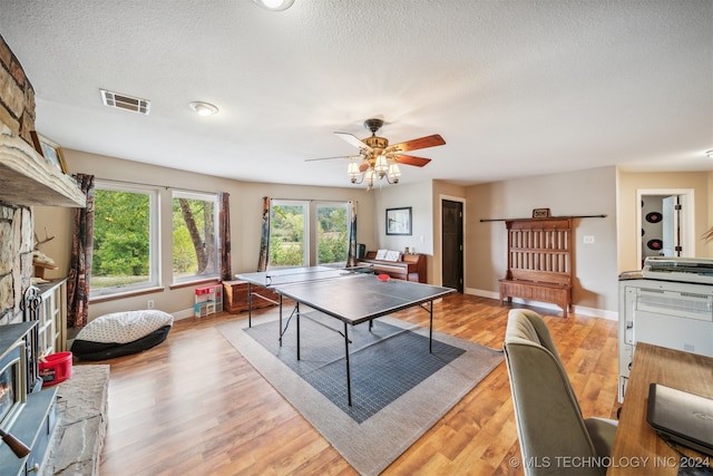 recreation room with ceiling fan, a textured ceiling, a fireplace, and light hardwood / wood-style floors