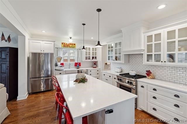 kitchen with white cabinets, pendant lighting, a kitchen island, stainless steel appliances, and dark hardwood / wood-style flooring