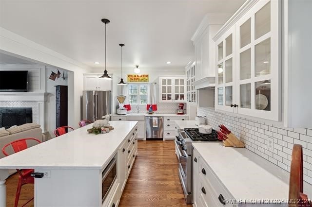 kitchen featuring a fireplace, white cabinets, appliances with stainless steel finishes, a kitchen bar, and tasteful backsplash