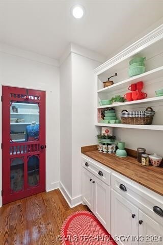 interior space with white cabinets, dark hardwood / wood-style floors, ornamental molding, and butcher block counters