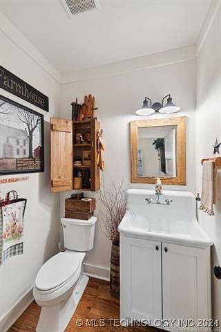 bathroom with wood-type flooring, vanity, crown molding, and toilet