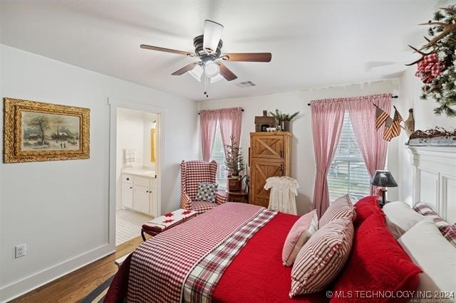 bedroom with ceiling fan, ensuite bath, multiple windows, and hardwood / wood-style floors