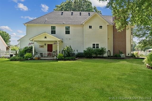 rear view of property featuring a lawn and fence