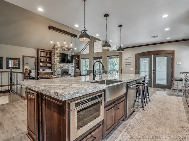 kitchen with hanging light fixtures, sink, a stone fireplace, a large island, and light hardwood / wood-style flooring