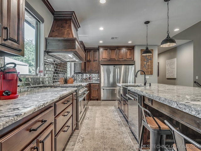 kitchen with hanging light fixtures, backsplash, stainless steel appliances, dark brown cabinets, and custom exhaust hood