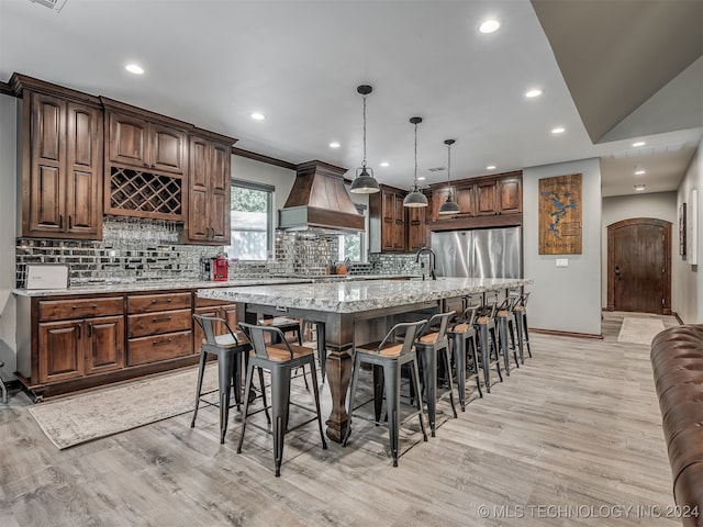 kitchen with custom exhaust hood, a large island, decorative light fixtures, light hardwood / wood-style flooring, and decorative backsplash