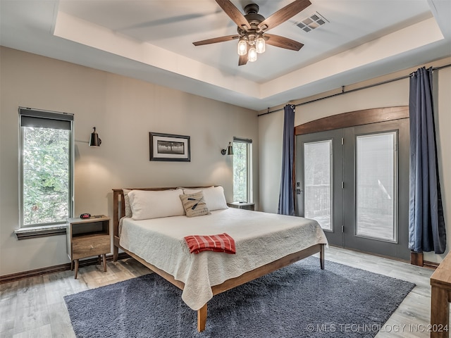 bedroom featuring access to outside, wood-type flooring, ceiling fan, and a raised ceiling