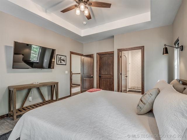 bedroom with light wood-type flooring, ensuite bath, ceiling fan, and a raised ceiling