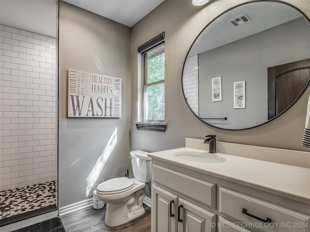 bathroom with a tile shower, vanity, toilet, and wood-type flooring