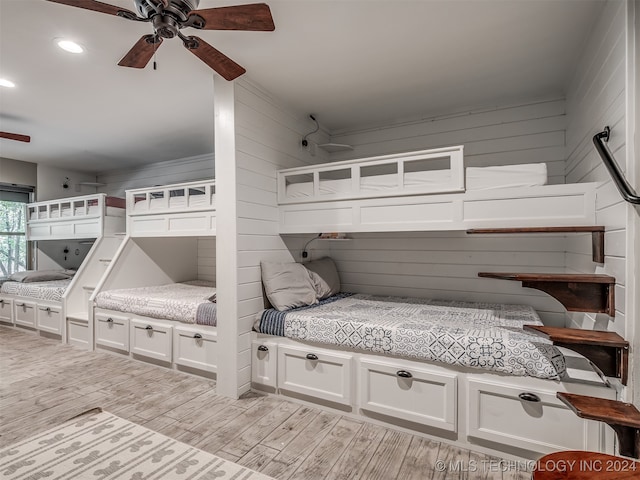 bedroom with light hardwood / wood-style flooring, wood walls, and ceiling fan