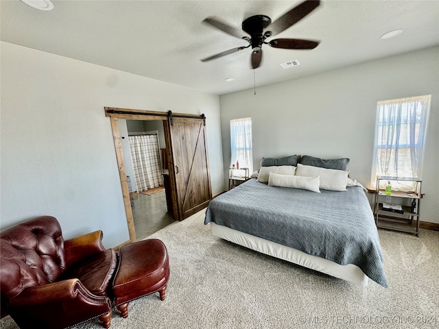 carpeted bedroom with a barn door and ceiling fan