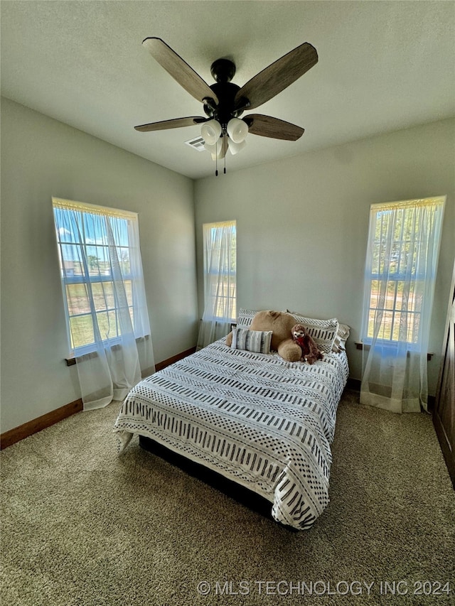 carpeted bedroom with a textured ceiling, multiple windows, and ceiling fan