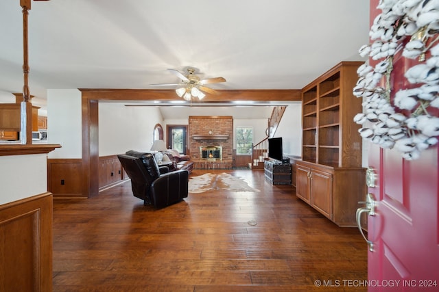 living room with a brick fireplace, ceiling fan, and dark wood-type flooring