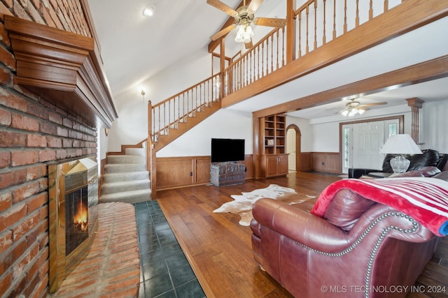 living room featuring ceiling fan, wood walls, wood-type flooring, and a fireplace