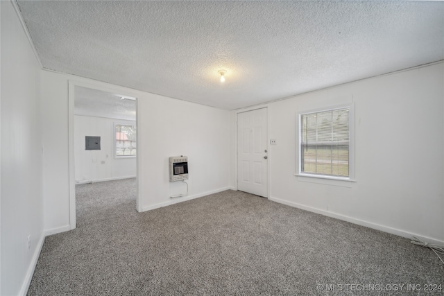 empty room with heating unit, electric panel, carpet flooring, and a textured ceiling