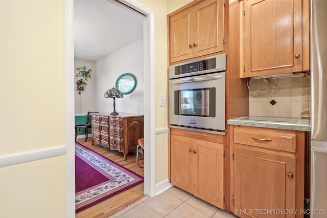 kitchen with decorative backsplash, light hardwood / wood-style floors, stovetop, and stainless steel oven