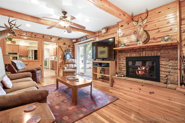 living room with beamed ceiling, a fireplace, ceiling fan, and light hardwood / wood-style flooring