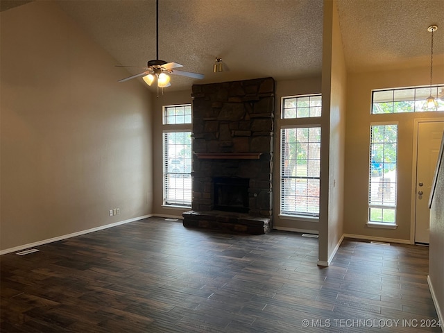 unfurnished living room featuring ceiling fan, a stone fireplace, dark hardwood / wood-style flooring, and a wealth of natural light