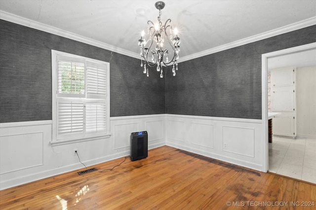 empty room featuring wood-type flooring, crown molding, and a chandelier