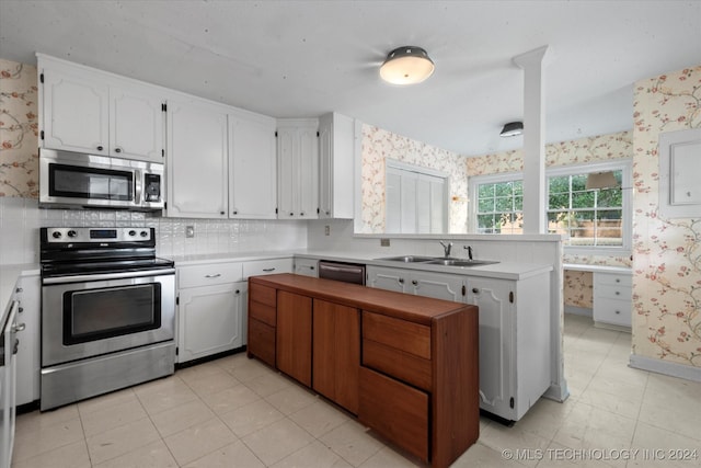 kitchen with tasteful backsplash, sink, white cabinets, kitchen peninsula, and appliances with stainless steel finishes