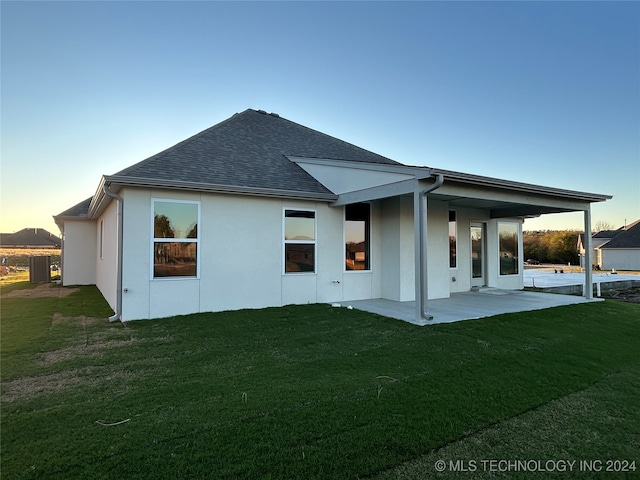 back house at dusk featuring a lawn and a patio area