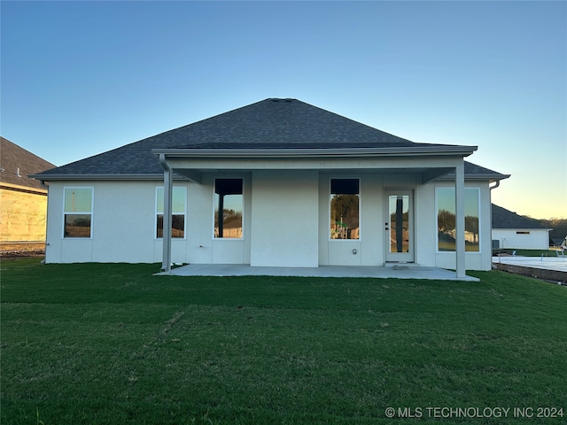 back house at dusk with a patio and a yard