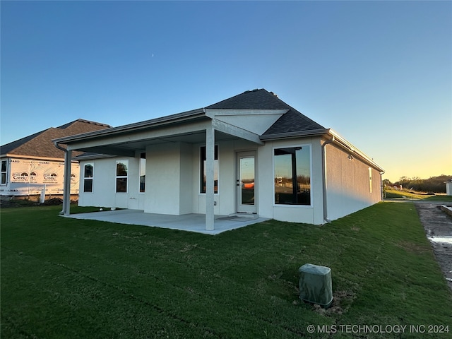 back house at dusk featuring a lawn and a patio