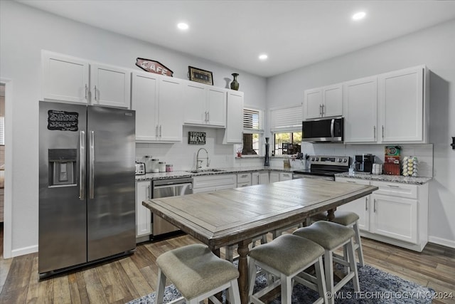 kitchen with light stone counters, sink, white cabinetry, stainless steel appliances, and dark hardwood / wood-style flooring