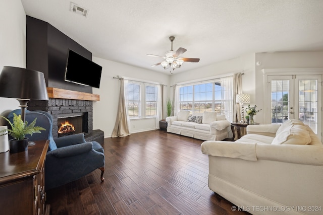 living room with a textured ceiling, dark wood-type flooring, a fireplace, ceiling fan, and french doors