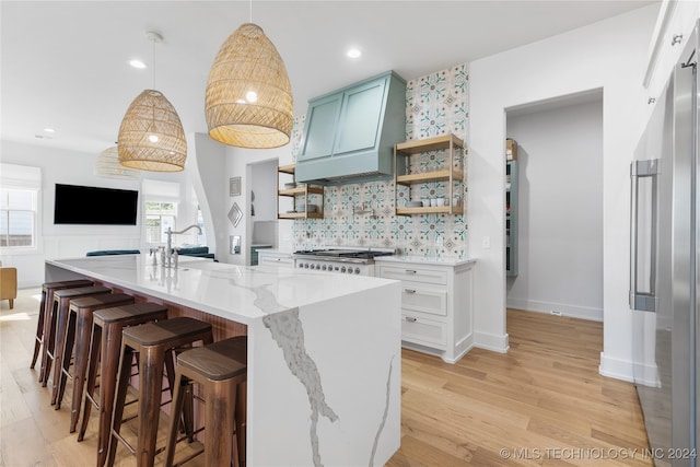 kitchen with light wood-type flooring, hanging light fixtures, stainless steel appliances, and custom range hood