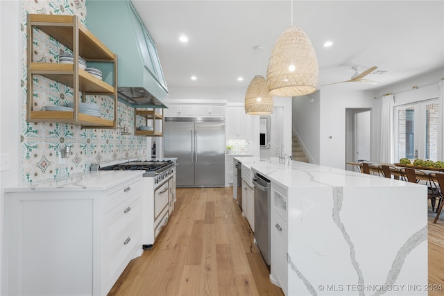 kitchen featuring pendant lighting, an island with sink, premium appliances, backsplash, and white cabinetry