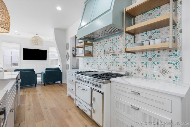 kitchen featuring white cabinetry, stainless steel gas stovetop, custom range hood, light stone countertops, and light hardwood / wood-style floors