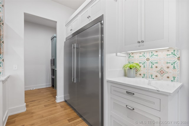 kitchen featuring light stone counters, white cabinets, built in refrigerator, light hardwood / wood-style flooring, and decorative backsplash