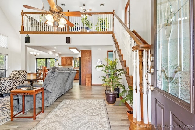 foyer entrance featuring ceiling fan with notable chandelier, light wood-type flooring, and high vaulted ceiling