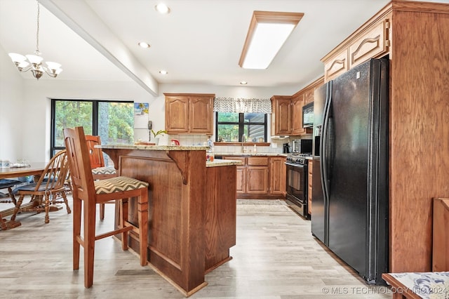 kitchen featuring black appliances, light hardwood / wood-style flooring, decorative light fixtures, light stone counters, and a chandelier