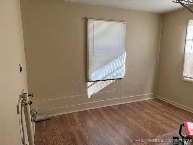 unfurnished room with baseboards, wood finished floors, and a textured wall