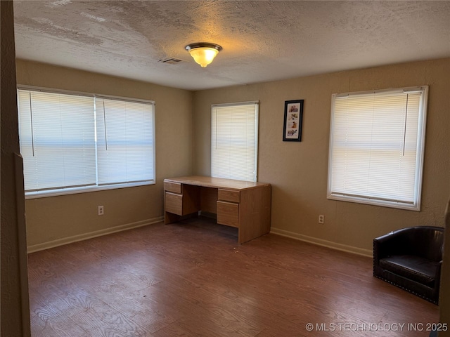 unfurnished office with a textured ceiling, wood finished floors, visible vents, and baseboards