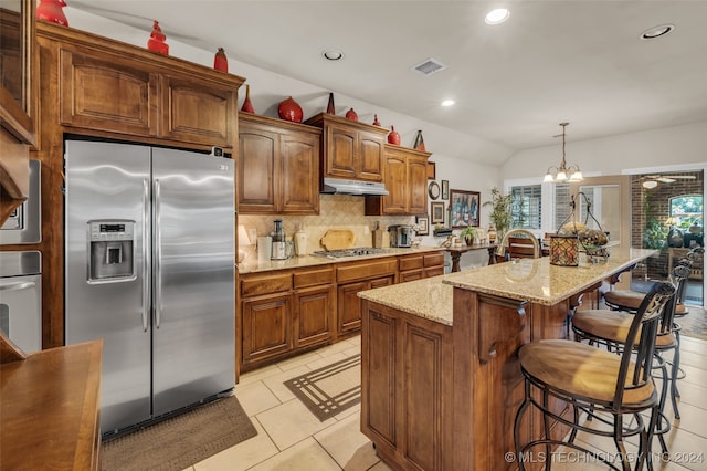 kitchen featuring an island with sink, pendant lighting, vaulted ceiling, decorative backsplash, and appliances with stainless steel finishes