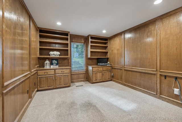 unfurnished office featuring light carpet, wooden walls, and built in desk