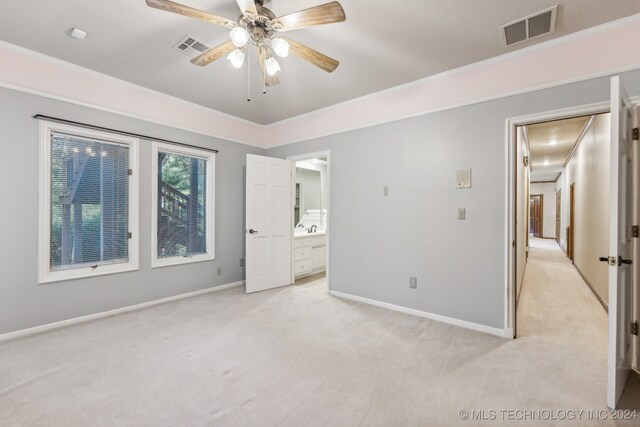 unfurnished bedroom featuring ceiling fan, crown molding, light colored carpet, sink, and ensuite bath