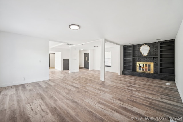 unfurnished living room featuring a brick fireplace, built in features, and hardwood / wood-style floors