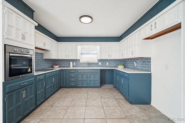 kitchen with black electric cooktop, decorative backsplash, blue cabinets, light tile patterned flooring, and oven