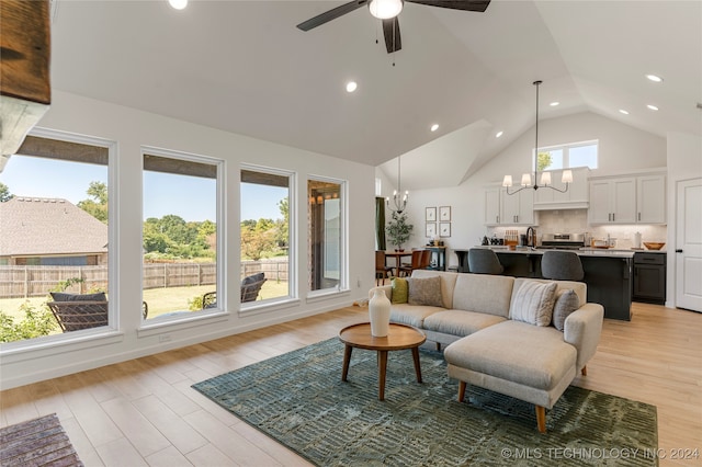 living room featuring ceiling fan with notable chandelier, light wood-type flooring, and high vaulted ceiling