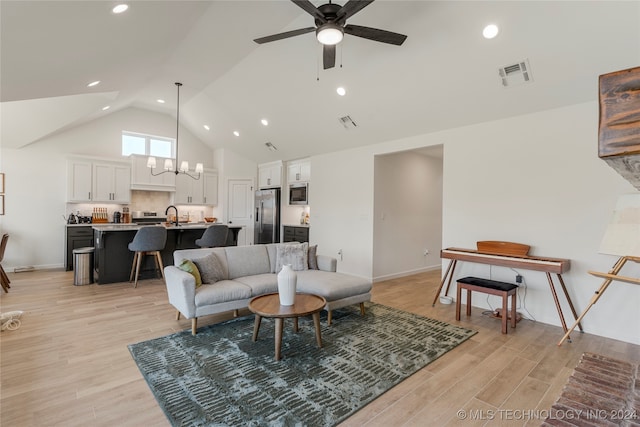 living room featuring ceiling fan with notable chandelier, light hardwood / wood-style floors, vaulted ceiling, and sink