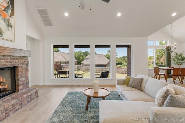 living room featuring a brick fireplace, ceiling fan with notable chandelier, light hardwood / wood-style floors, and high vaulted ceiling