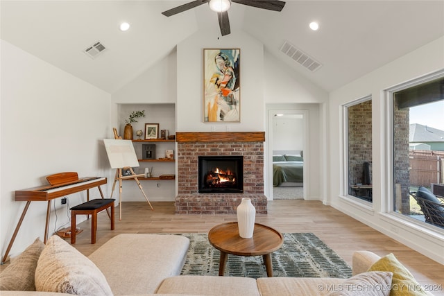 living room featuring ceiling fan, light hardwood / wood-style flooring, a brick fireplace, and high vaulted ceiling